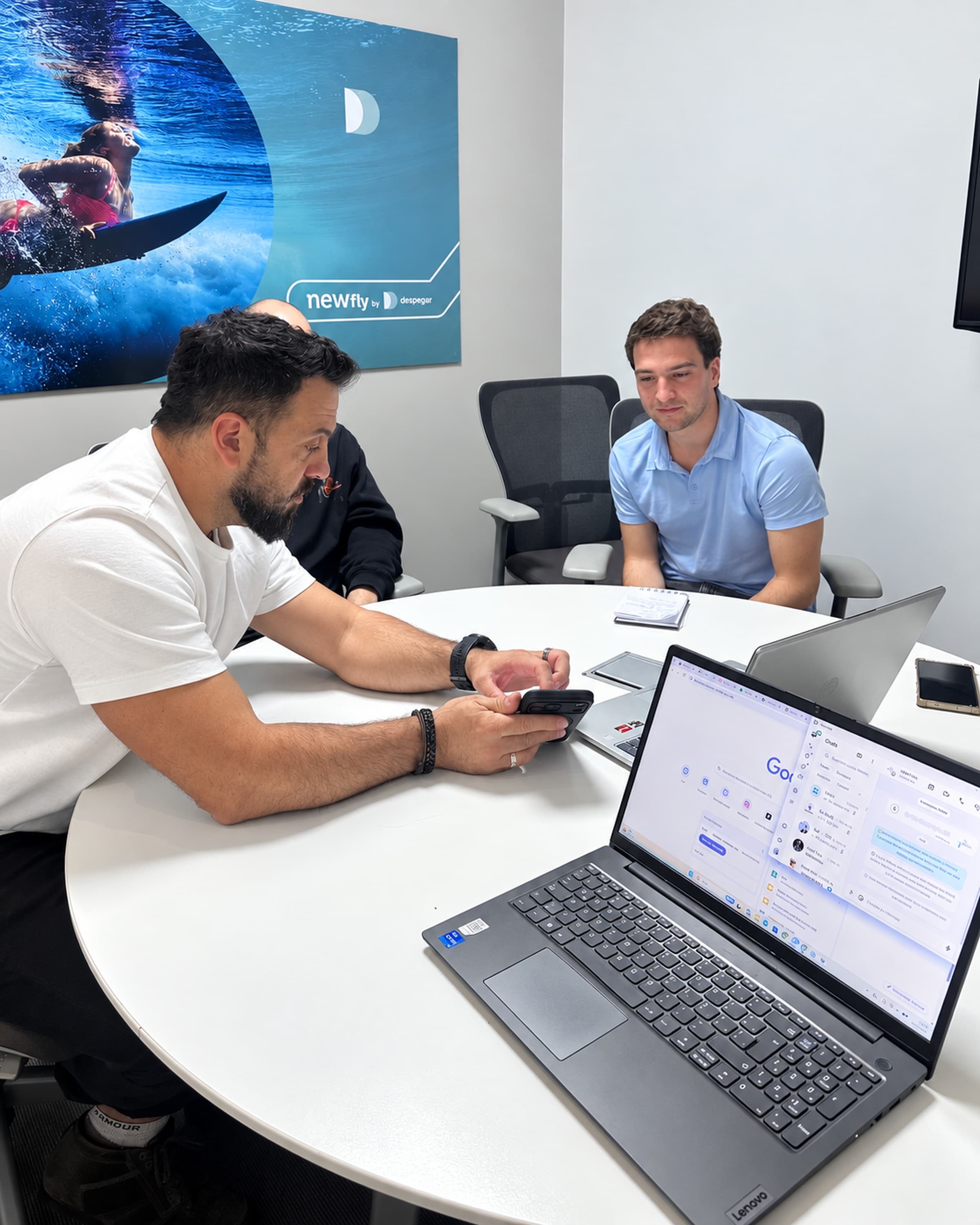Tres personas del equipo de LIA y del cliente trabajan alrededor de una mesa con notebooks y un celular en una oficina
